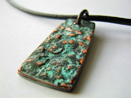 Hammered copper with verdegris patina. Each pendant is unique. This one was textured by hammering a pitted piece of rusty steel against the copper to leave an impression. They are then edge-textured and stamped with my mark before undergoing patination and final highlighting with fine abrasives. 
 Sealed in microcrystalline wax and hung on a leather cord.
 