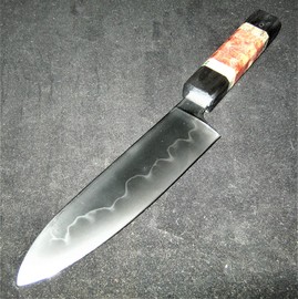 This is a Santoku, a Japanese-inspired kitchen knife with Western-style double-bevel grind of differentially hardened W2 tool steel and an edge of 63-64 Rockwell hardness.
 It is of 'hidden tang' construction, meaning that the blade steel extends the full length of the handle, and is pinned from the pommel to secure the stack of handle materials.